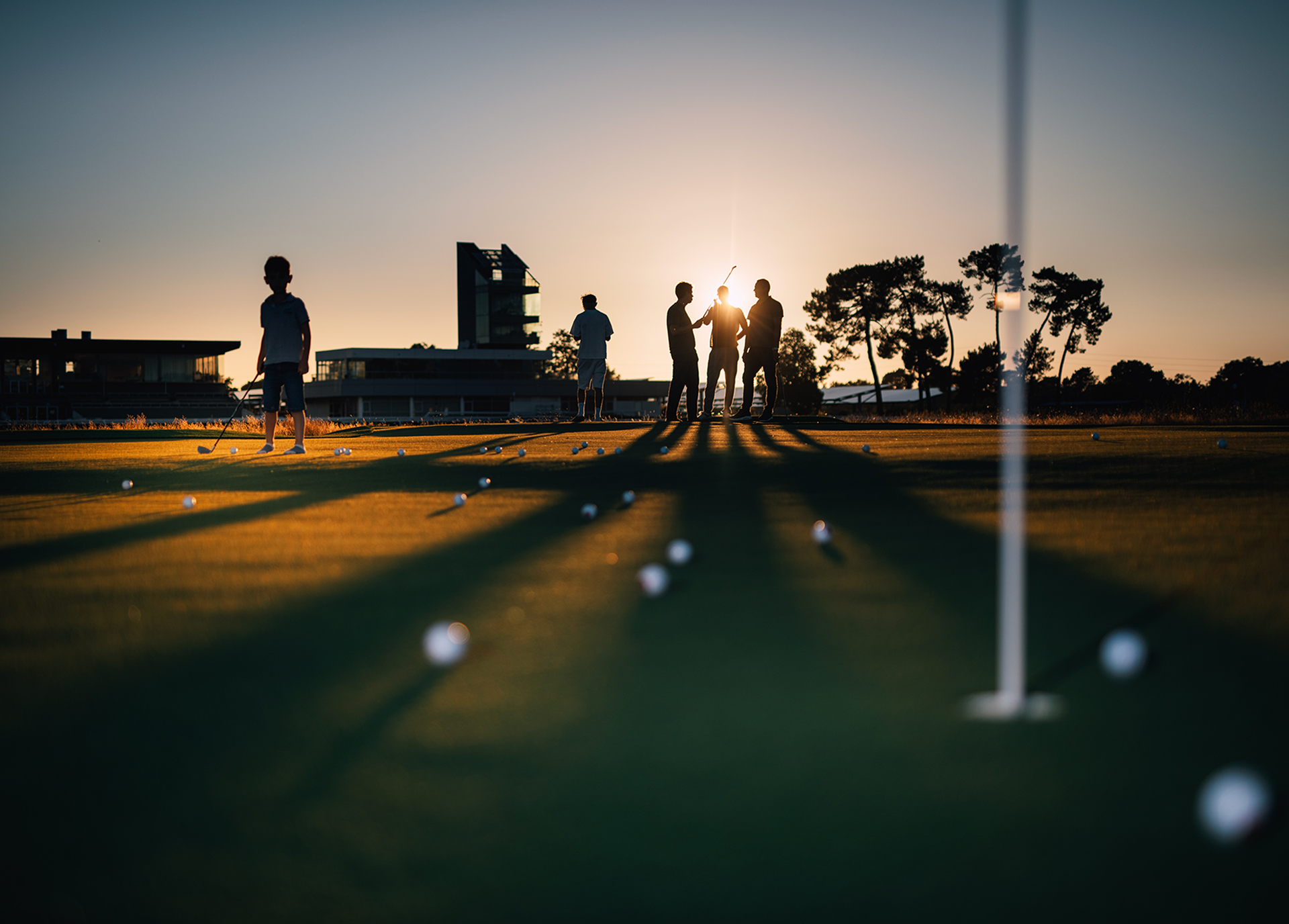 Un groupe de personnes et un enfant font du golf face au soleil qui se couche.